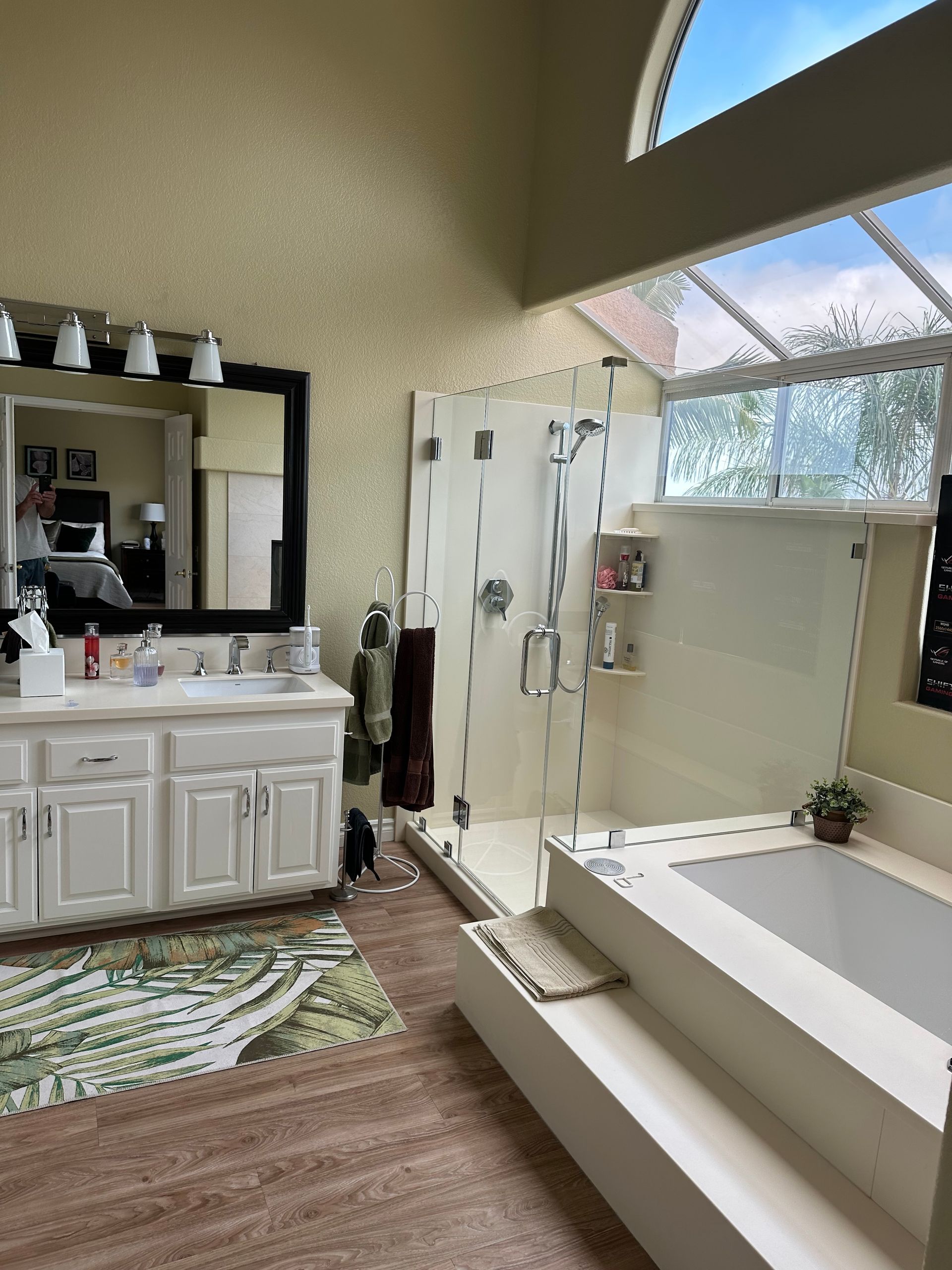 Modern bathroom with double vanity, glass shower, freestanding tub, and large arched window.