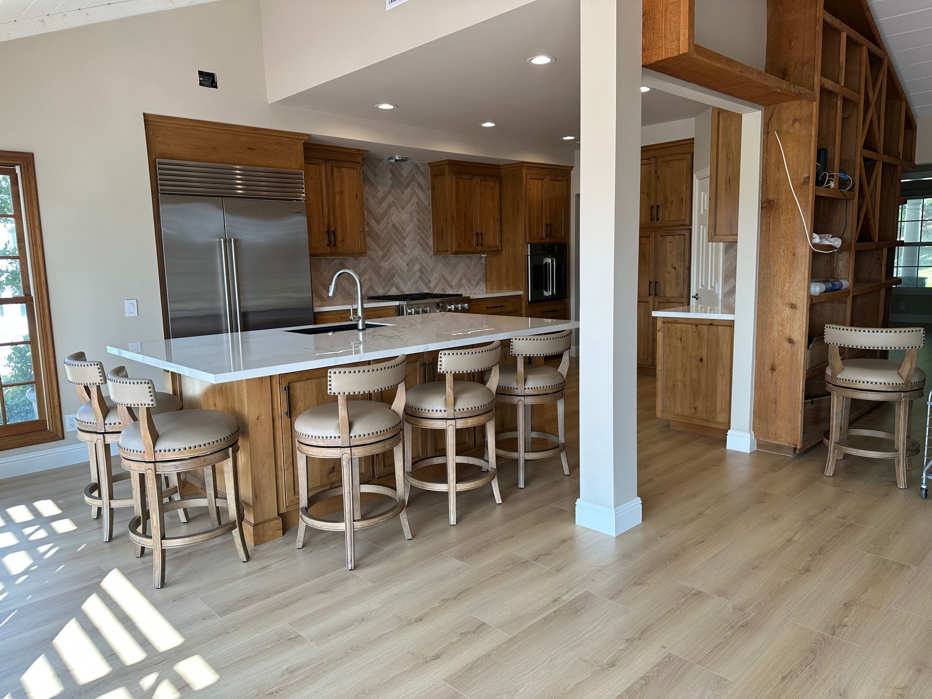 Bright modern kitchen with wood cabinets, large island, bar stools, and open dining area.
