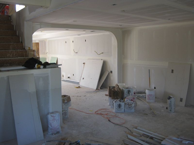 Renovation site with drywall leaning against a wall, tools and buckets scattered across a bare room