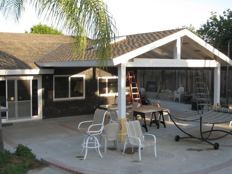 Backyard patio with white chairs, table, hammock, ladder, and a house with an open covered porch.