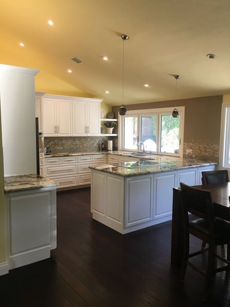 Bright modern kitchen with white cabinets, dark floors, island, and a window over the sink