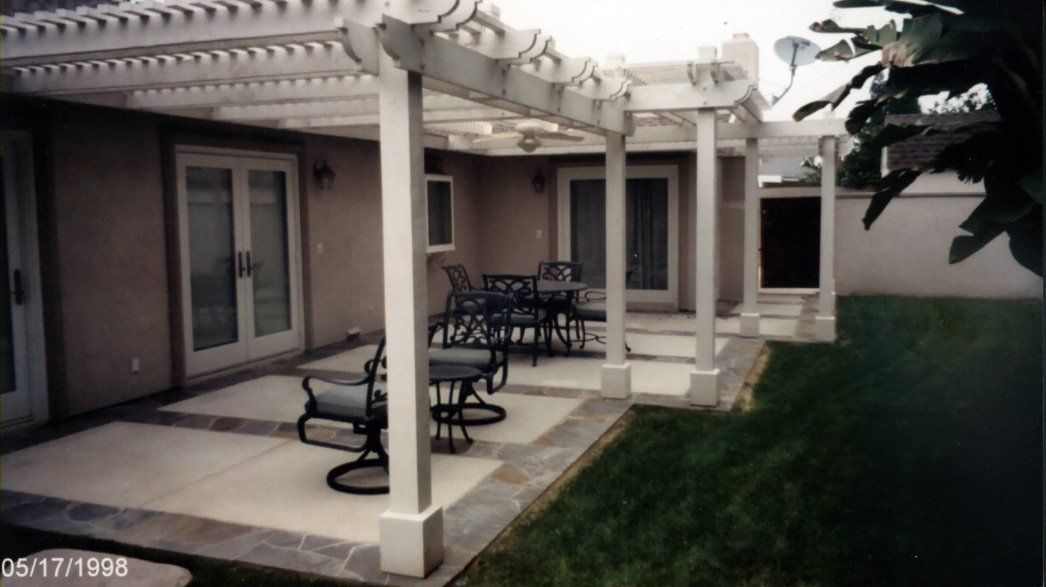 Covered patio with columns, outdoor tables and chairs beside a grassy yard