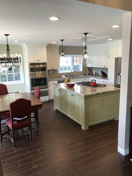 Bright kitchen with island, white cabinets, dark wood floor, and dining table by a window