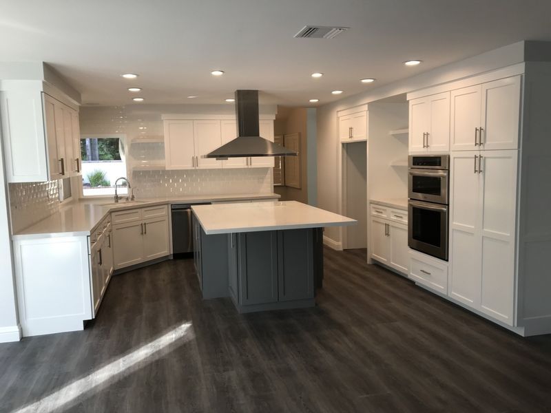 Modern white kitchen with dark island, stainless hood, and built-in ovens