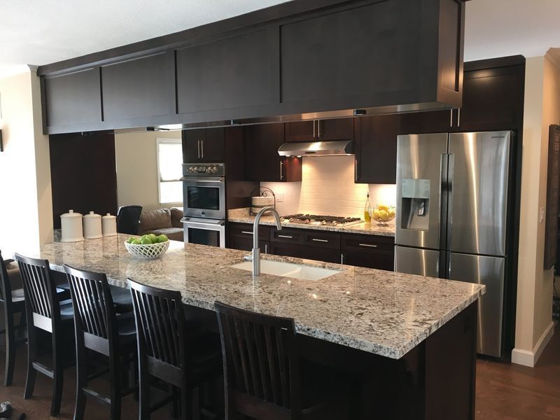 Modern kitchen with dark cabinets, granite island, stainless appliances, and bar stools