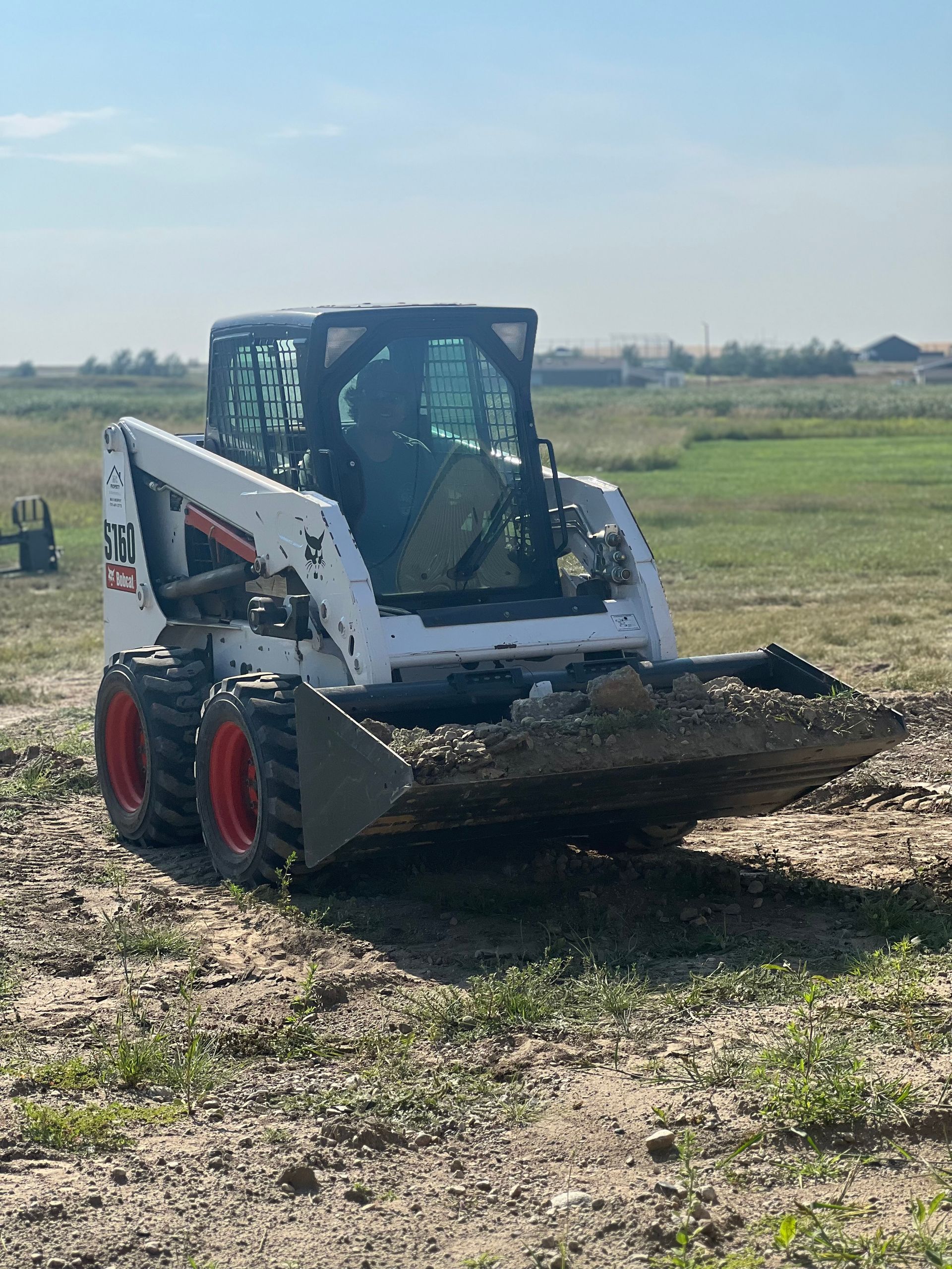 A bobcat skid steer is driving through a dirt field.