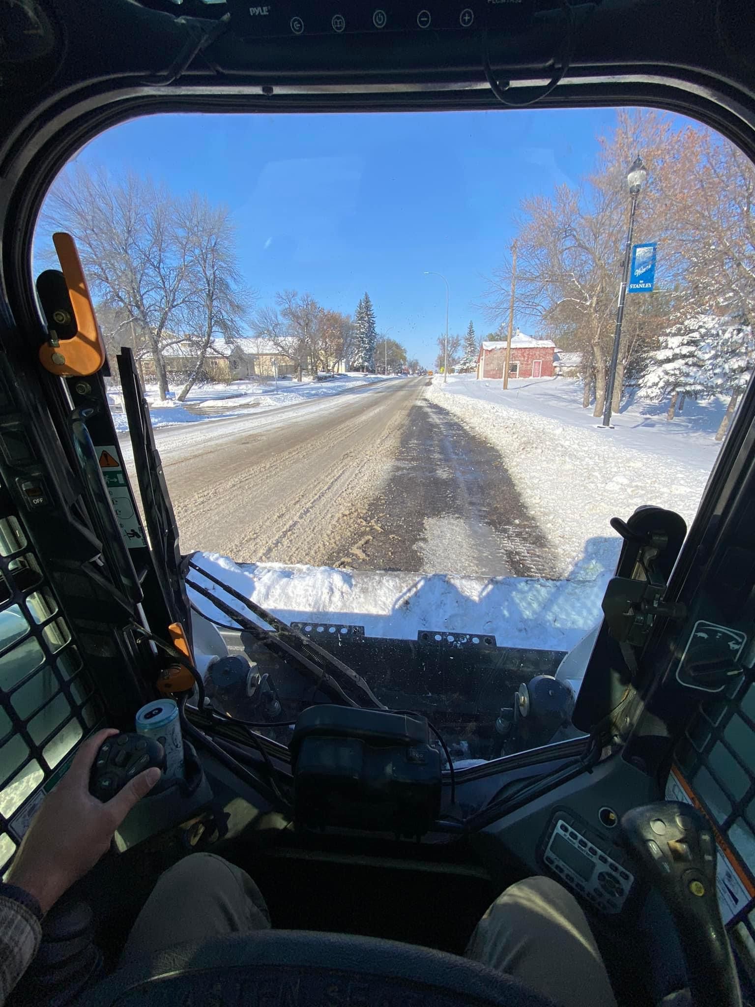 A person is driving a snow plow on a snowy road.