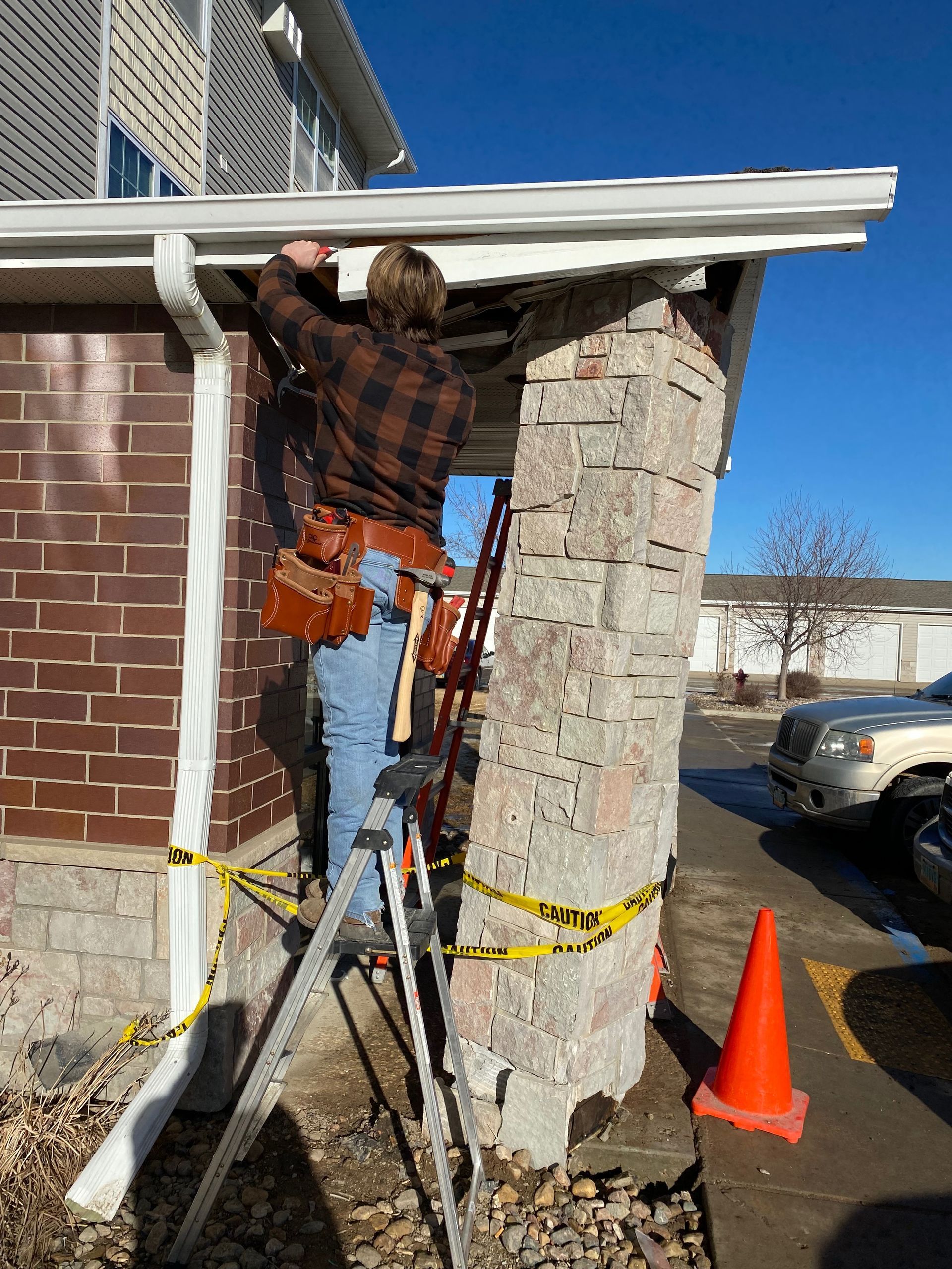 A man is standing on a ladder fixing a gutter on the side of a house.