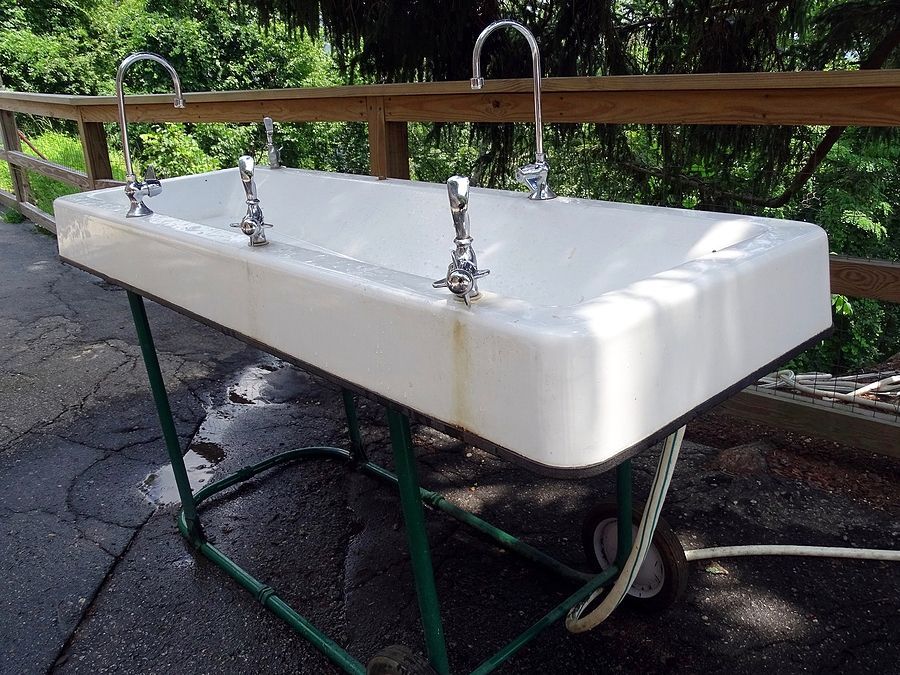 A white sink with chrome faucets sits on a green stand