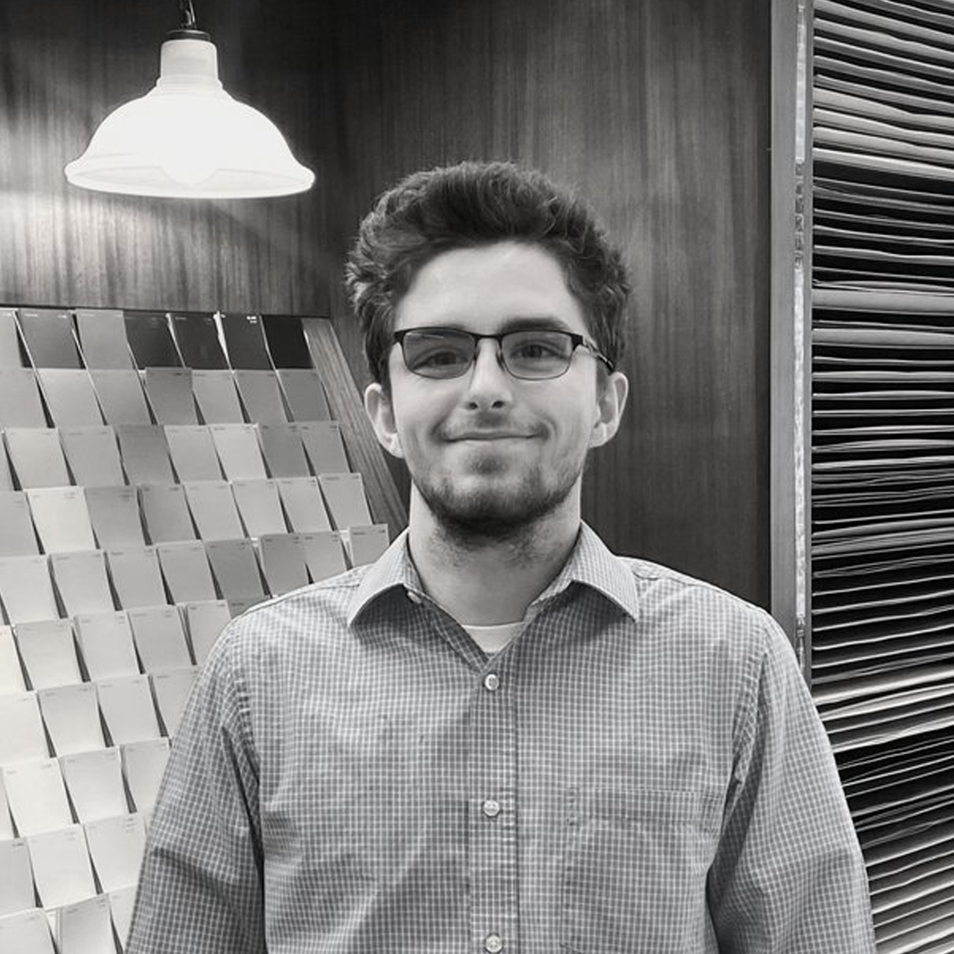 A black and white photo of a man wearing glasses and a plaid shirt.