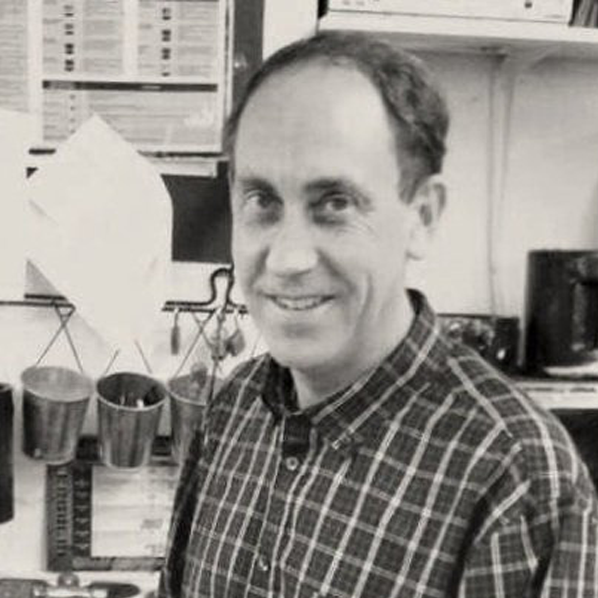 A man in a plaid shirt is smiling in a black and white photo.