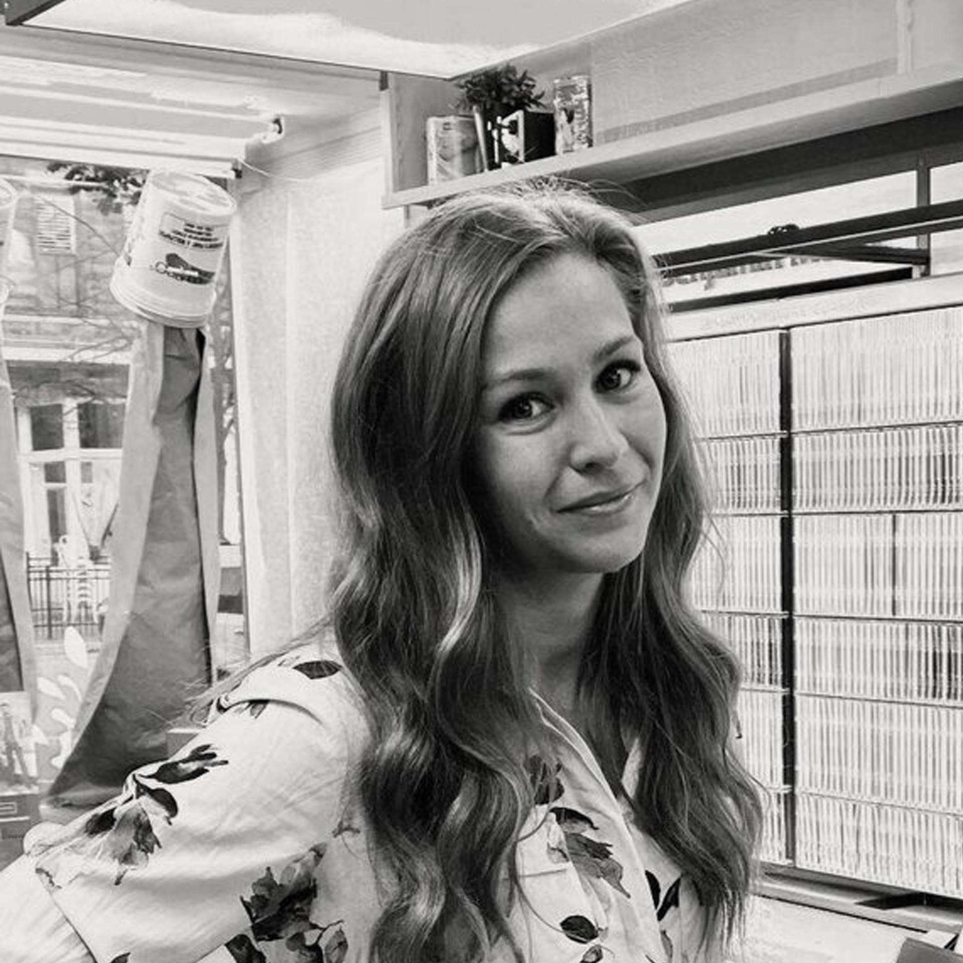 A black and white photo of a woman standing in front of a window.