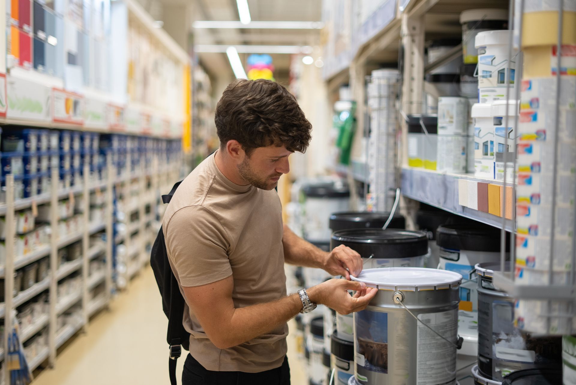 Person examines a paint can label in a store aisle lined with paint supplies.