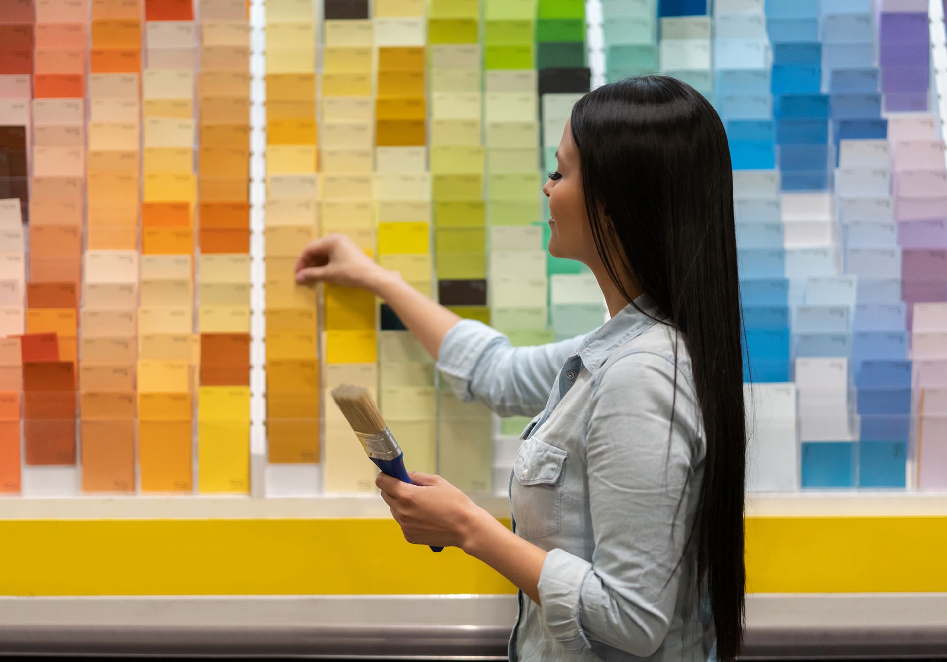 Woman choosing paint color from a display of swatches, holding a paintbrush.