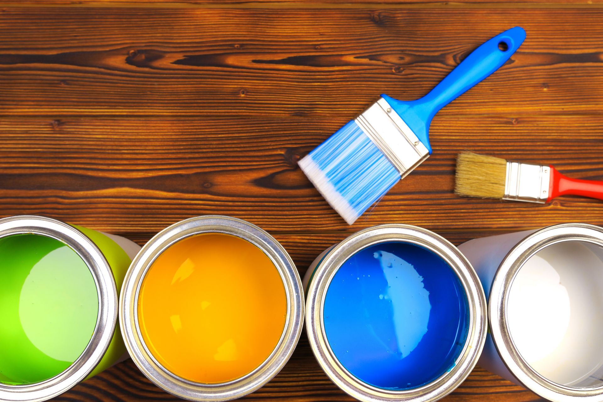 Four open paint cans with brushes on a dark wood surface.