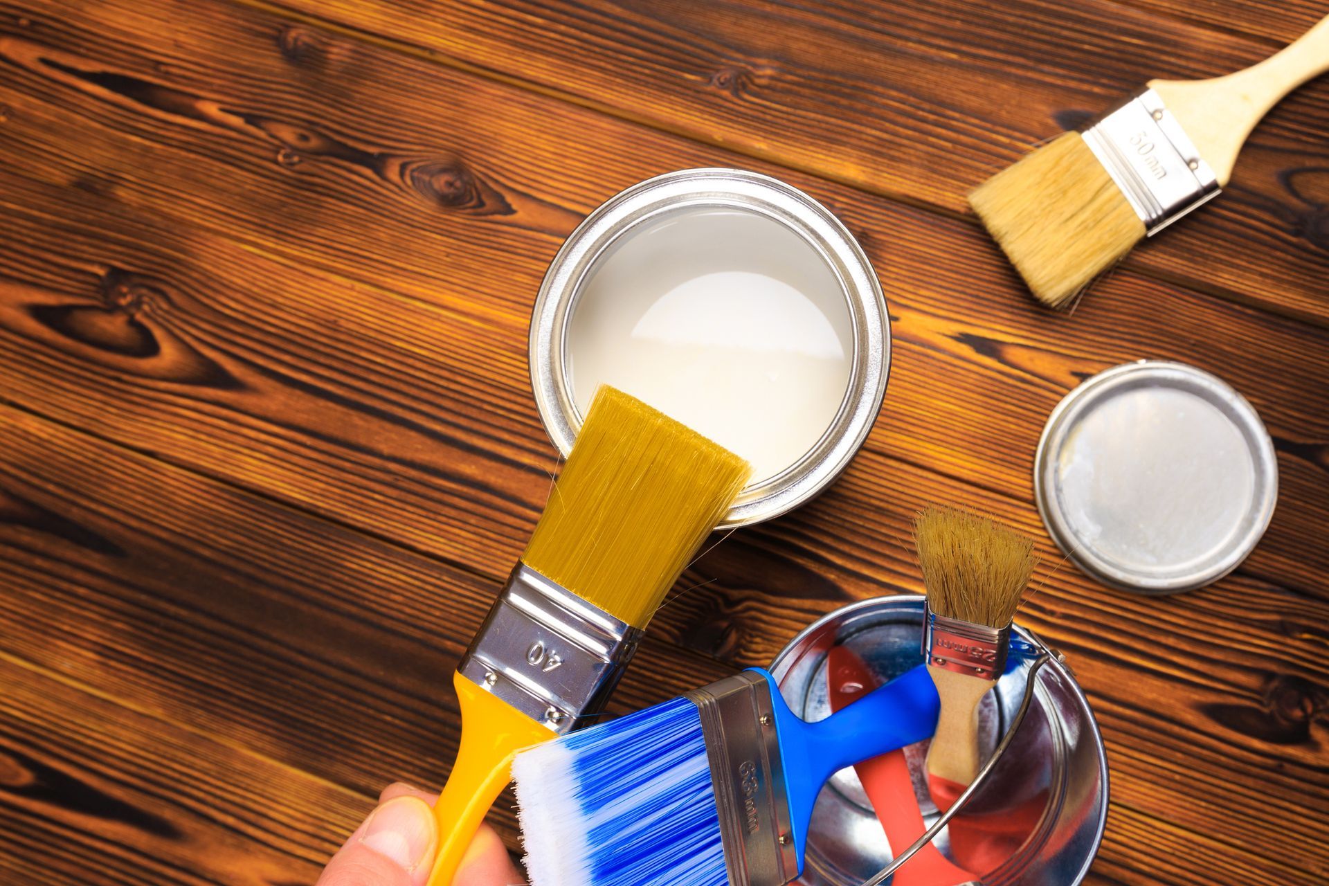 Paintbrushes and an open white paint can on a polished wooden surface.