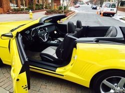 Yellow convertible car with black interior; door open on brick street.