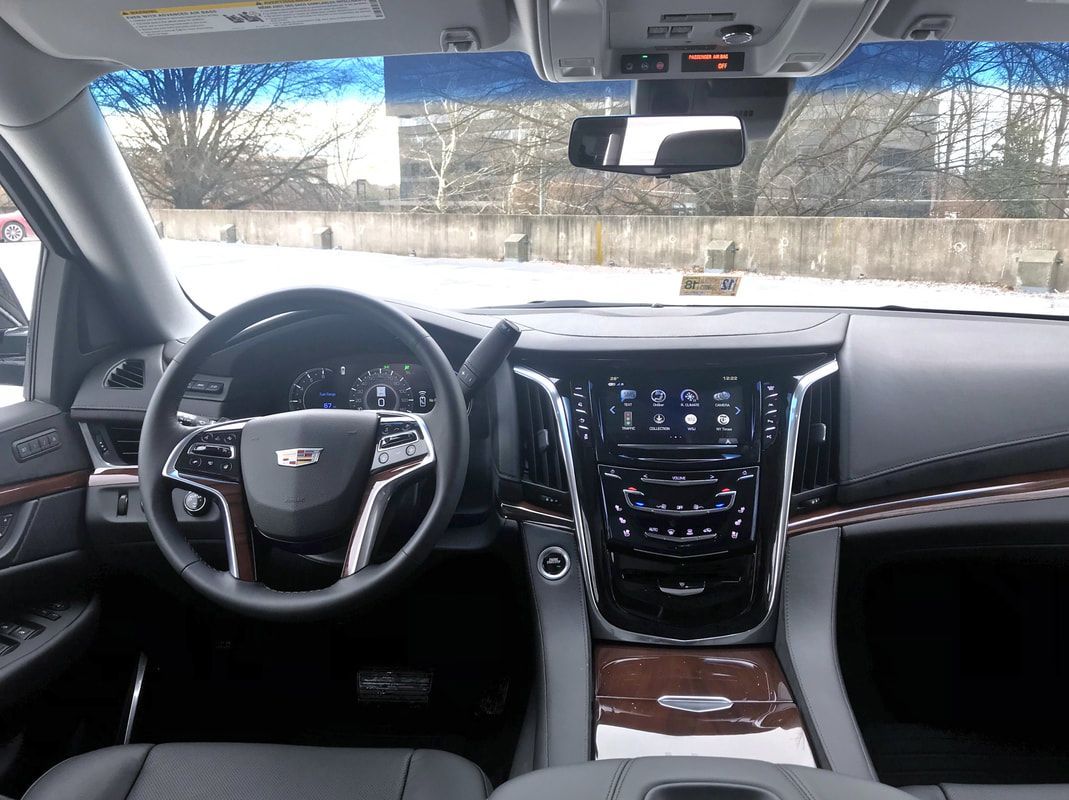 Interior view of a black Cadillac SUV with wood trim, featuring dashboard, steering wheel, and display screen.