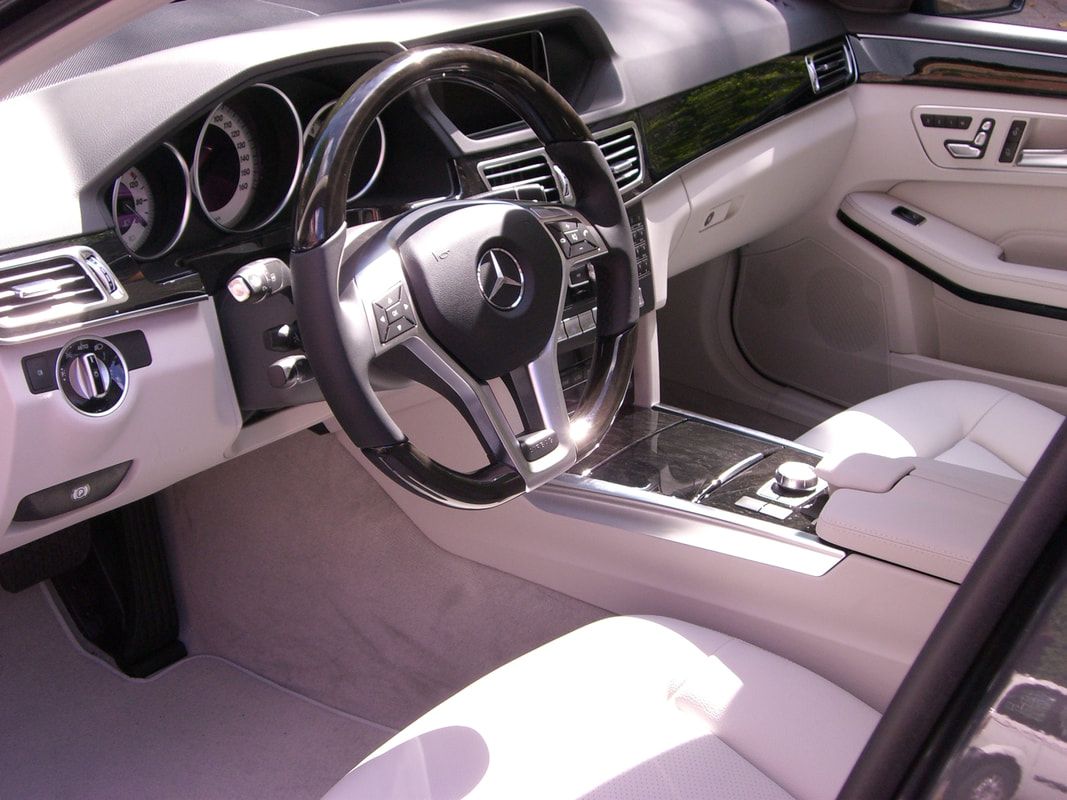 Mercedes-Benz car interior with white leather seats, a black and wood-grain dashboard, and a black steering wheel.