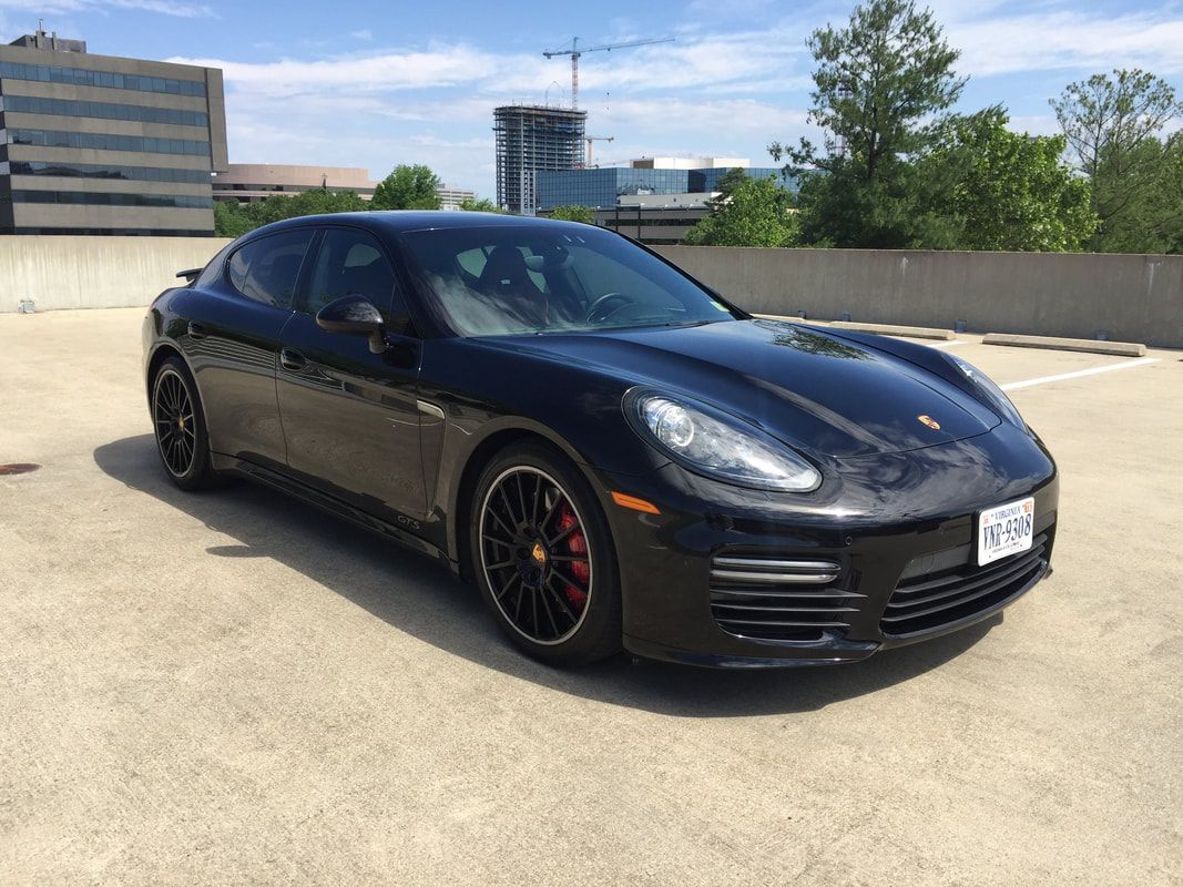 Black Porsche Panamera parked on a concrete rooftop parking lot, red brake calipers visible, sunny day.