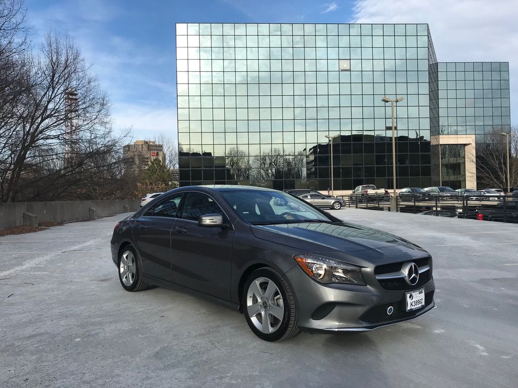 Gray Mercedes-Benz sedan parked on ice in front of a modern glass building.
