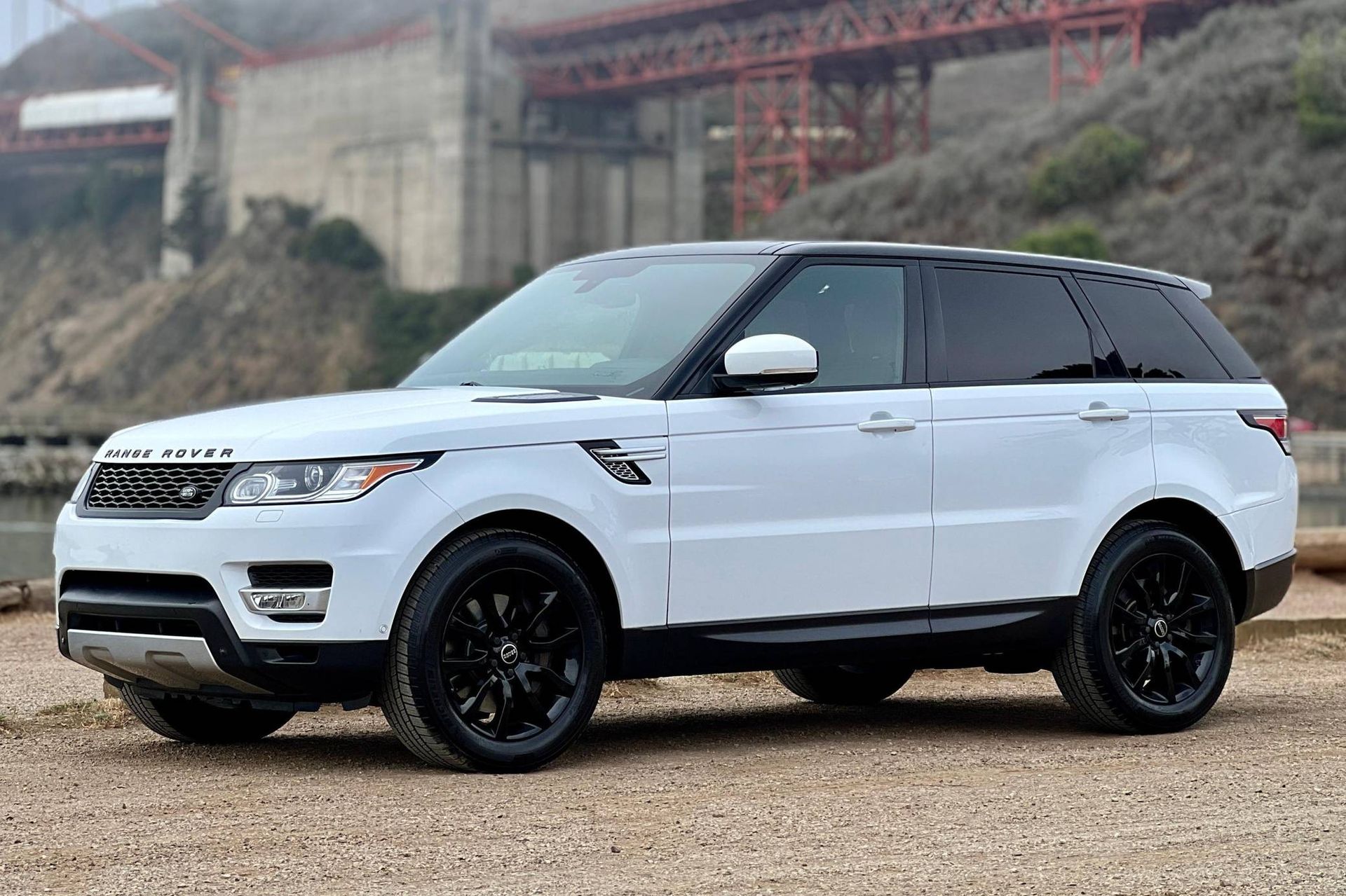 White Range Rover Sport SUV with black rims parked in front of a bridge.