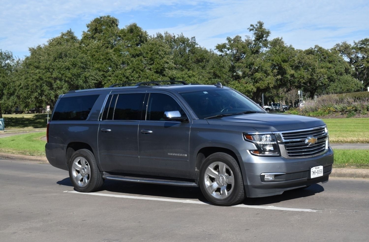 Gray Chevrolet Tahoe SUV parked on asphalt road, trees in the background.