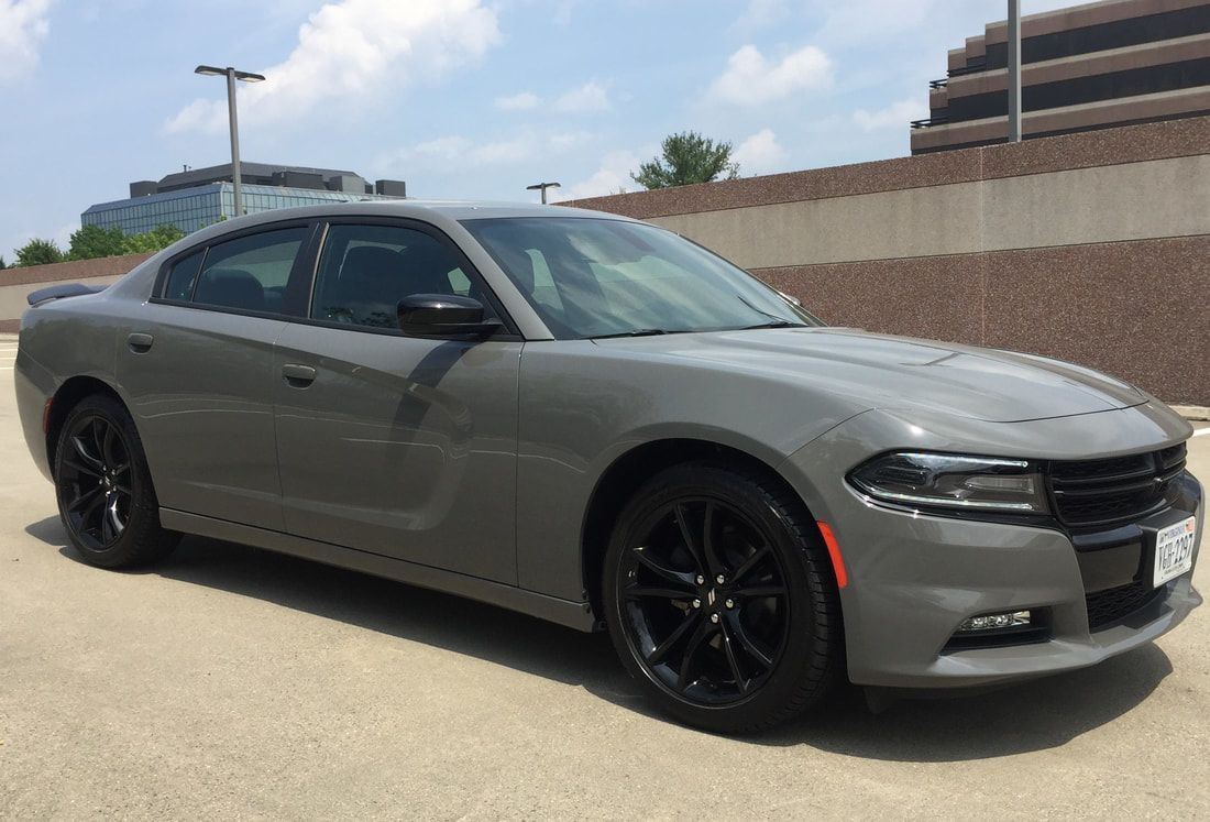 Gray Dodge Charger with black wheels parked on a paved lot in front of a building.