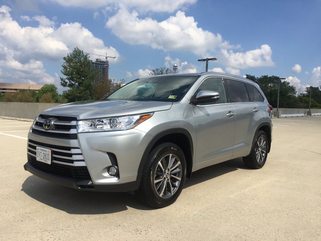 Silver Toyota Highlander SUV parked on a rooftop parking lot under a cloudy sky.