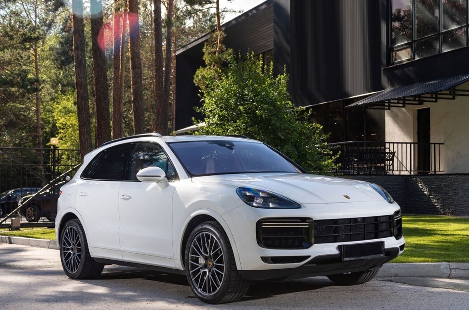 White Porsche SUV parked in front of a modern house, sunny day.