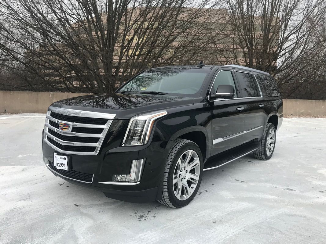 Black Cadillac Escalade SUV parked on snow-covered ground in front of a building with bare trees.