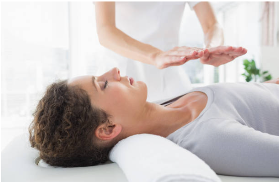 Photo demonstrating a reiki session with the provider's hands hovering over a fully clad patient.