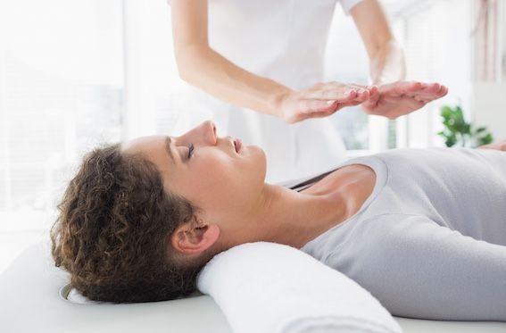 Photo demonstrating a reiki session with the provider's hands hovering over a fully clad patient.
