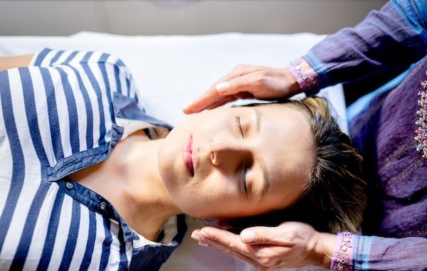Photo demonstrating a reiki session with the provider's hands hovering beside the client's head.