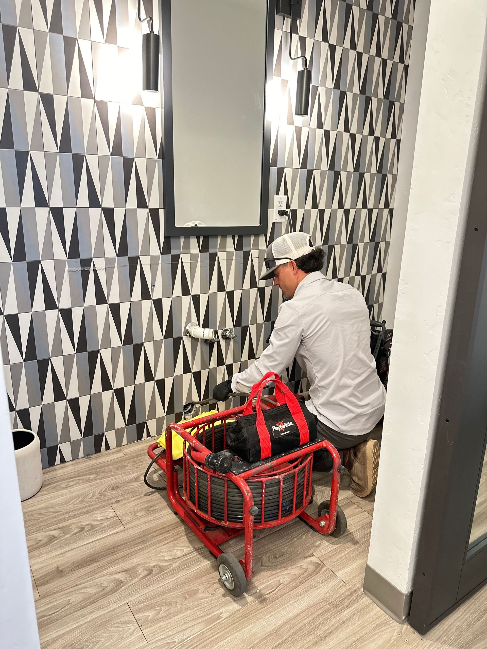 A man is sitting on the floor in a bathroom using a drain cleaner.