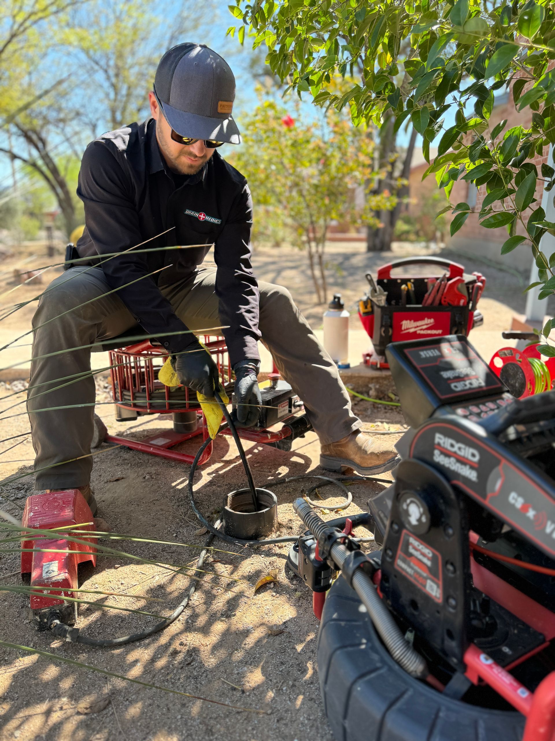 A man is kneeling down in the dirt working on a machine.