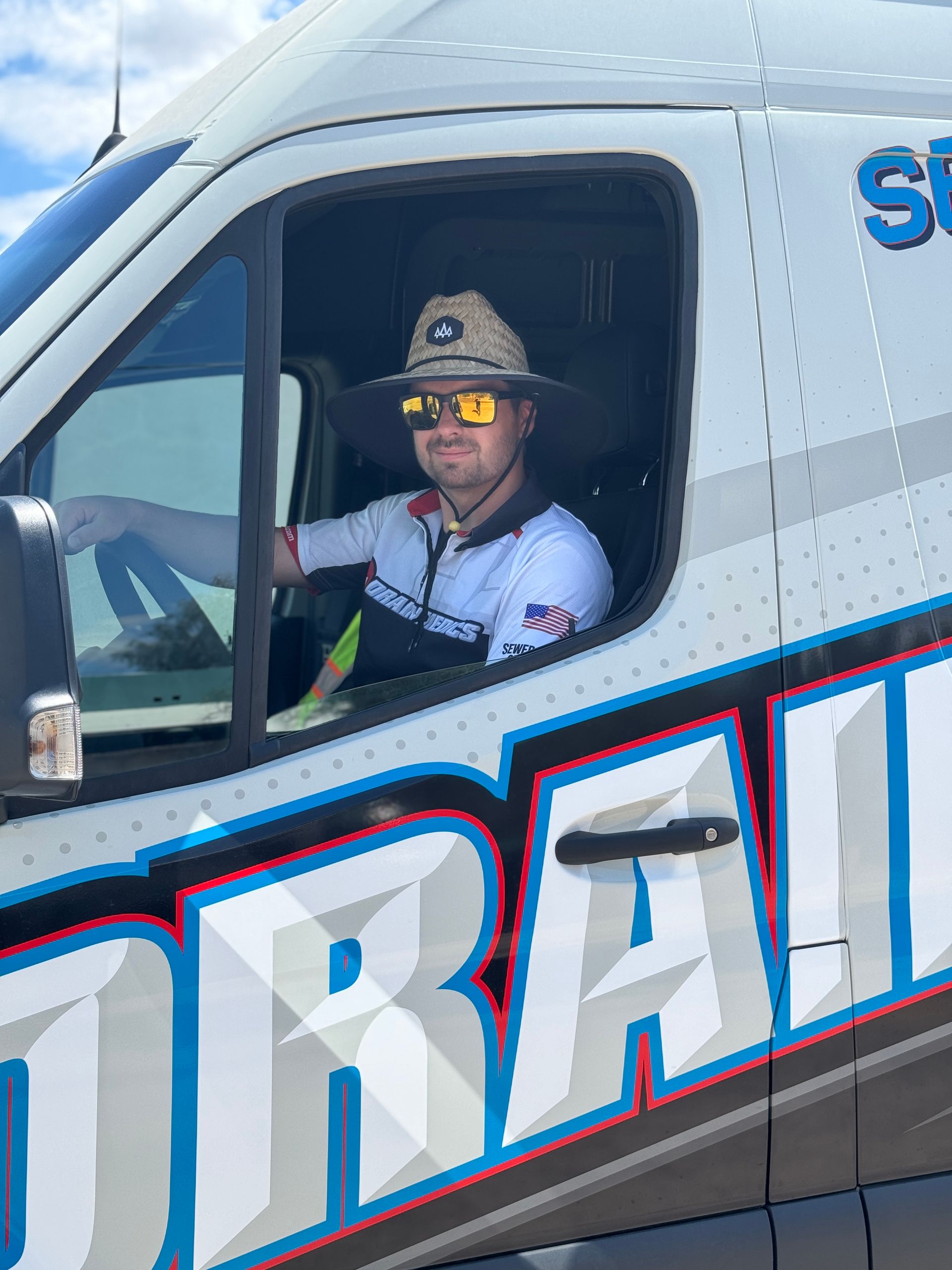 A man wearing a hat and sunglasses is sitting in the driver 's seat of a truck.
