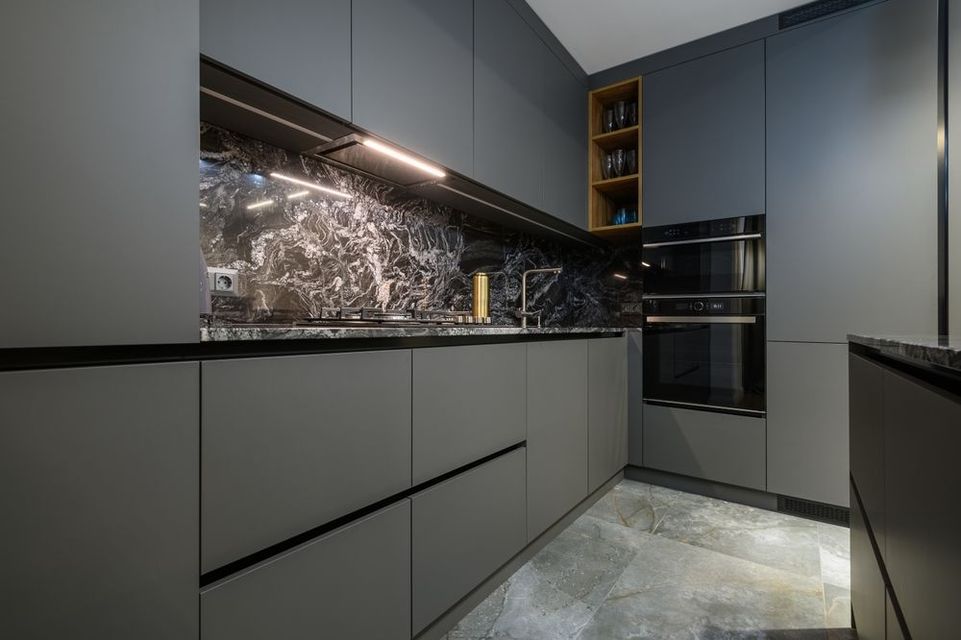 A modern kitchen with gray cabinets and black counter tops.