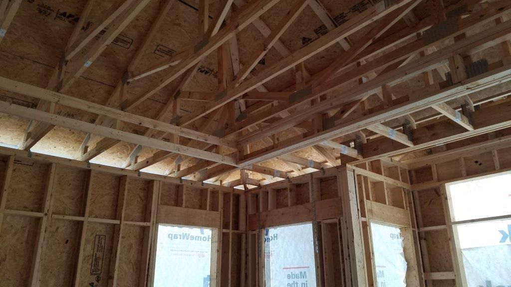 The inside of a house under construction with wooden beams and windows.