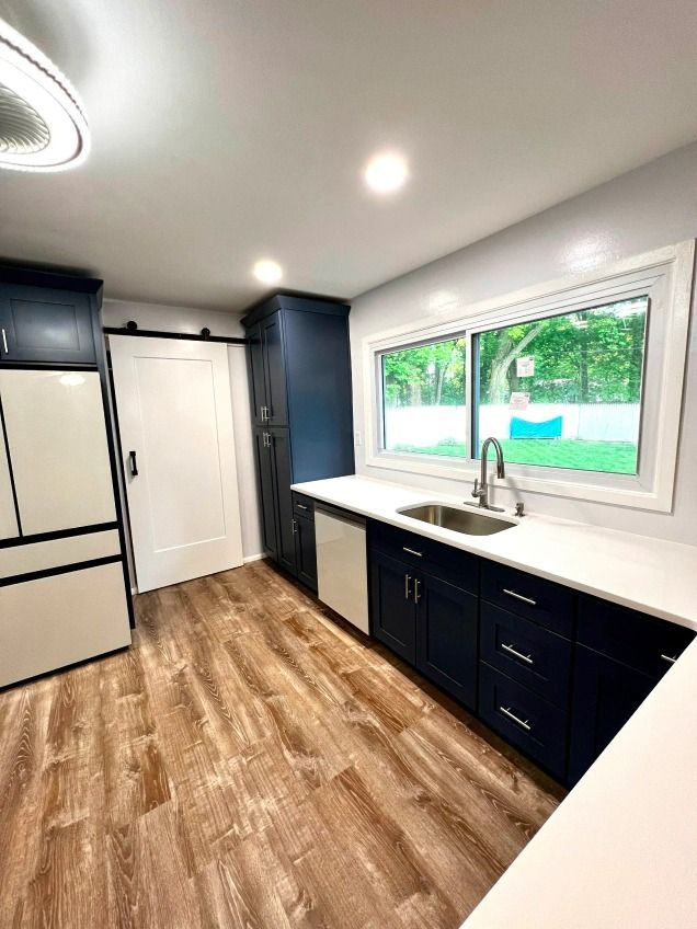 A kitchen with blue cabinets , white counter tops , a sink and a refrigerator.