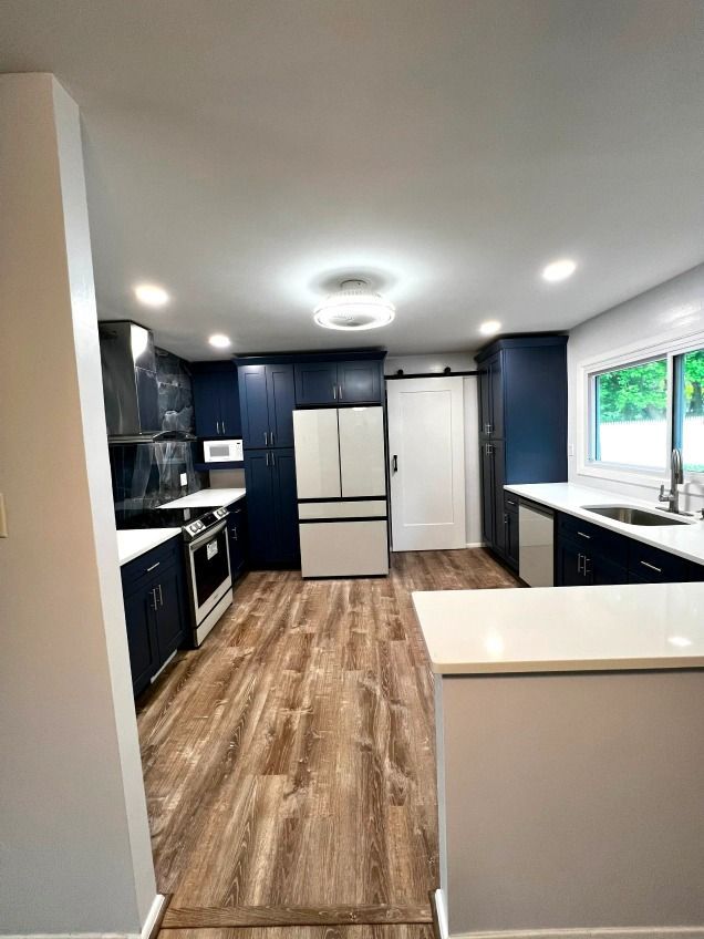 A kitchen with blue cabinets , white counter tops , stainless steel appliances , a refrigerator and a sink.