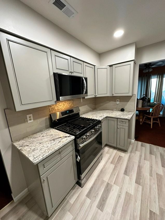 A kitchen with white cabinets , a stove and a microwave.