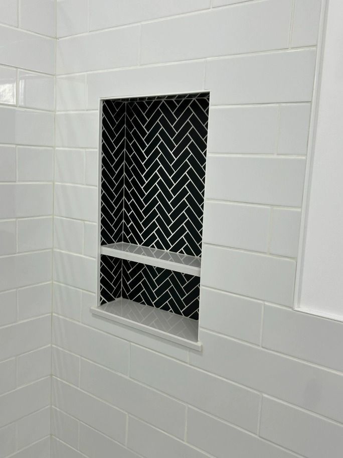A shower niche with a black and white herringbone pattern on the wall.