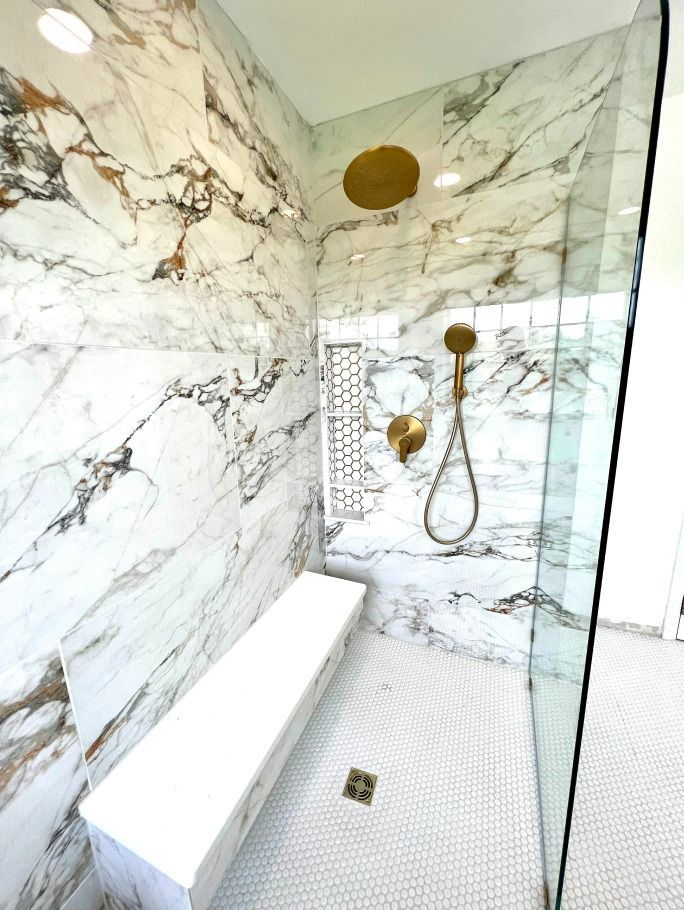 A bathroom with marble walls and a walk in shower with a bench.
