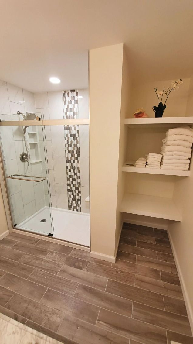 A bathroom with a walk in shower and shelves filled with towels.