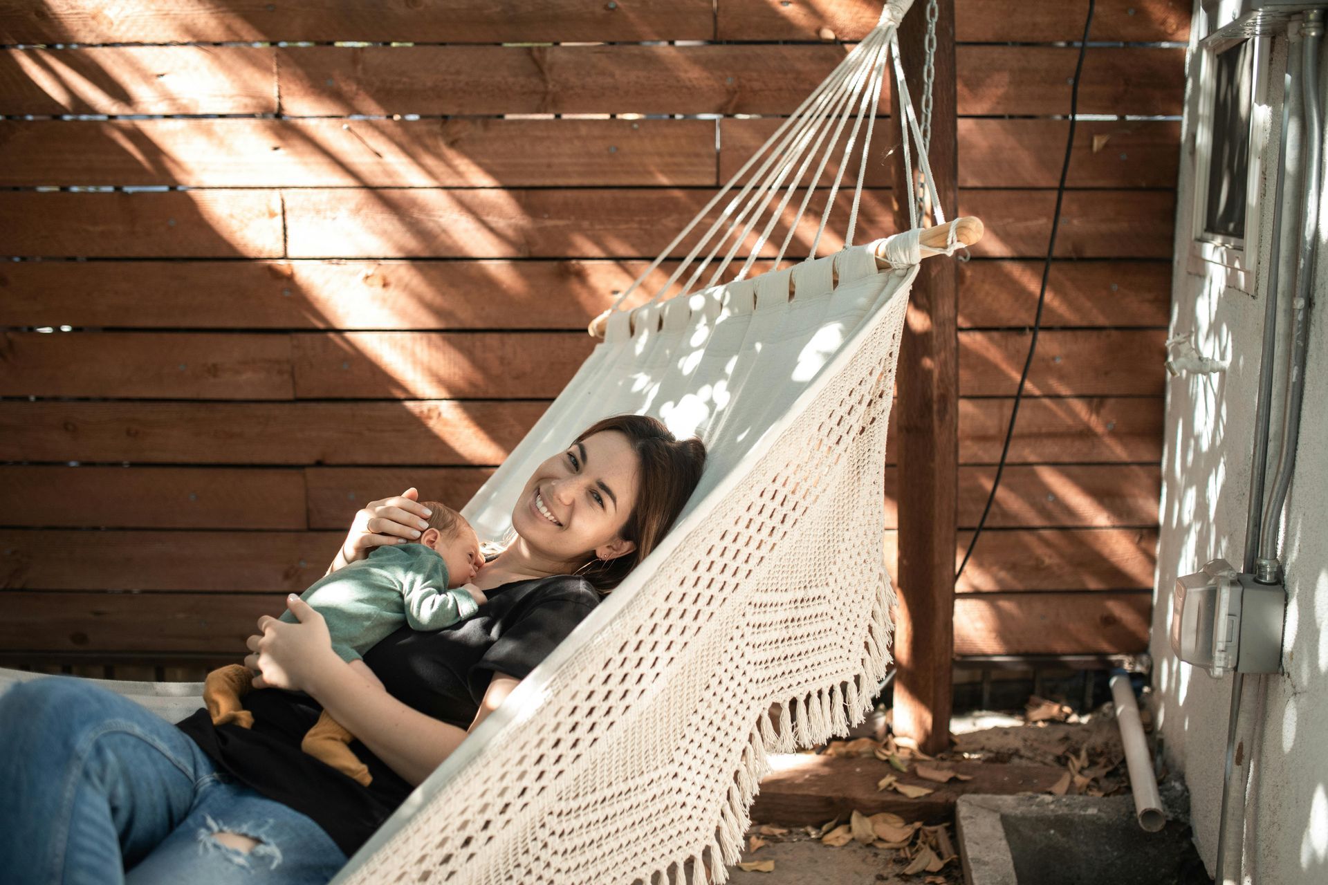 A woman is laying in a hammock holding a baby.