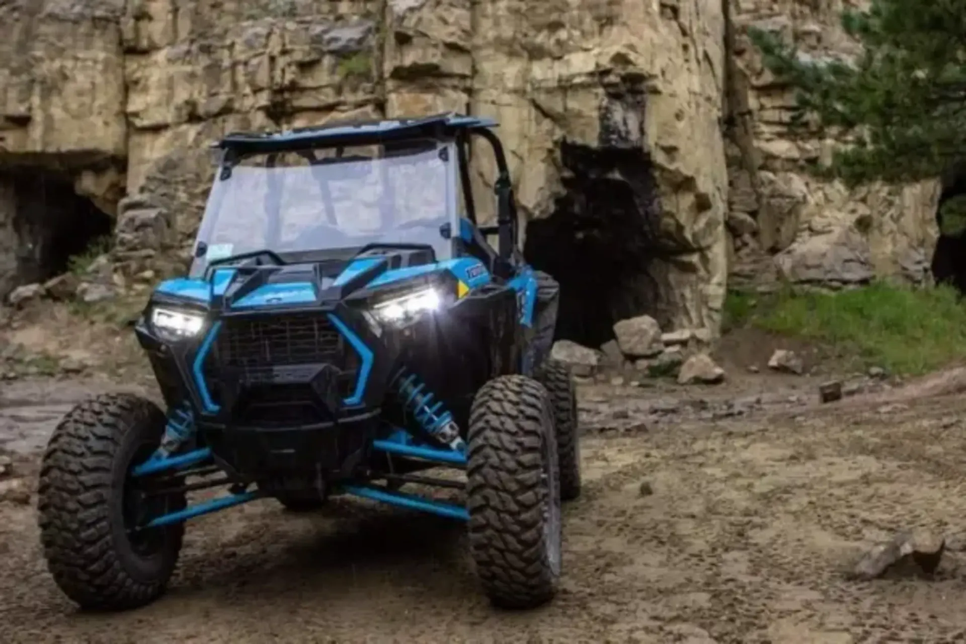 A blue atv is parked in the dirt in front of a cave.