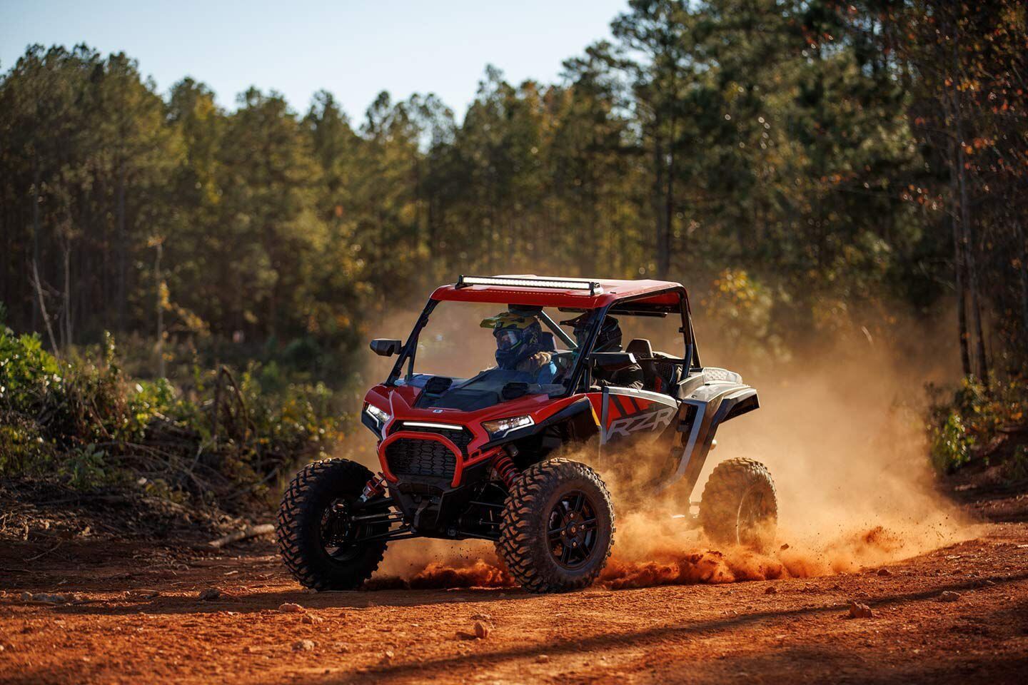 A red atv is driving down a dirt road in the woods.