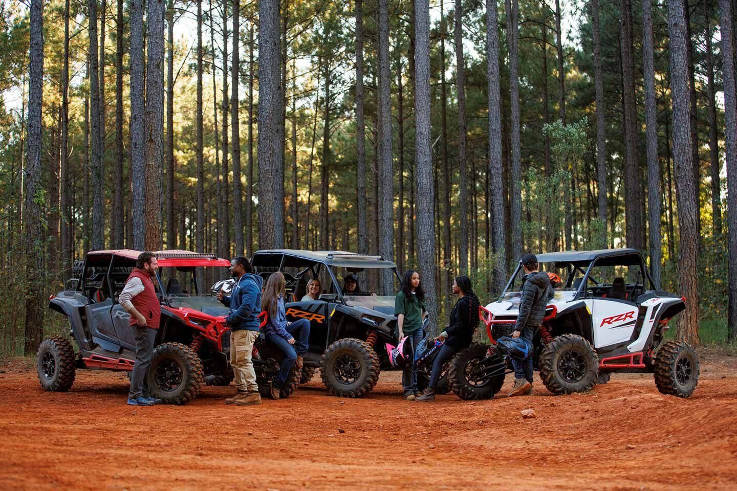 A group of people are standing next to atvs in the woods.
