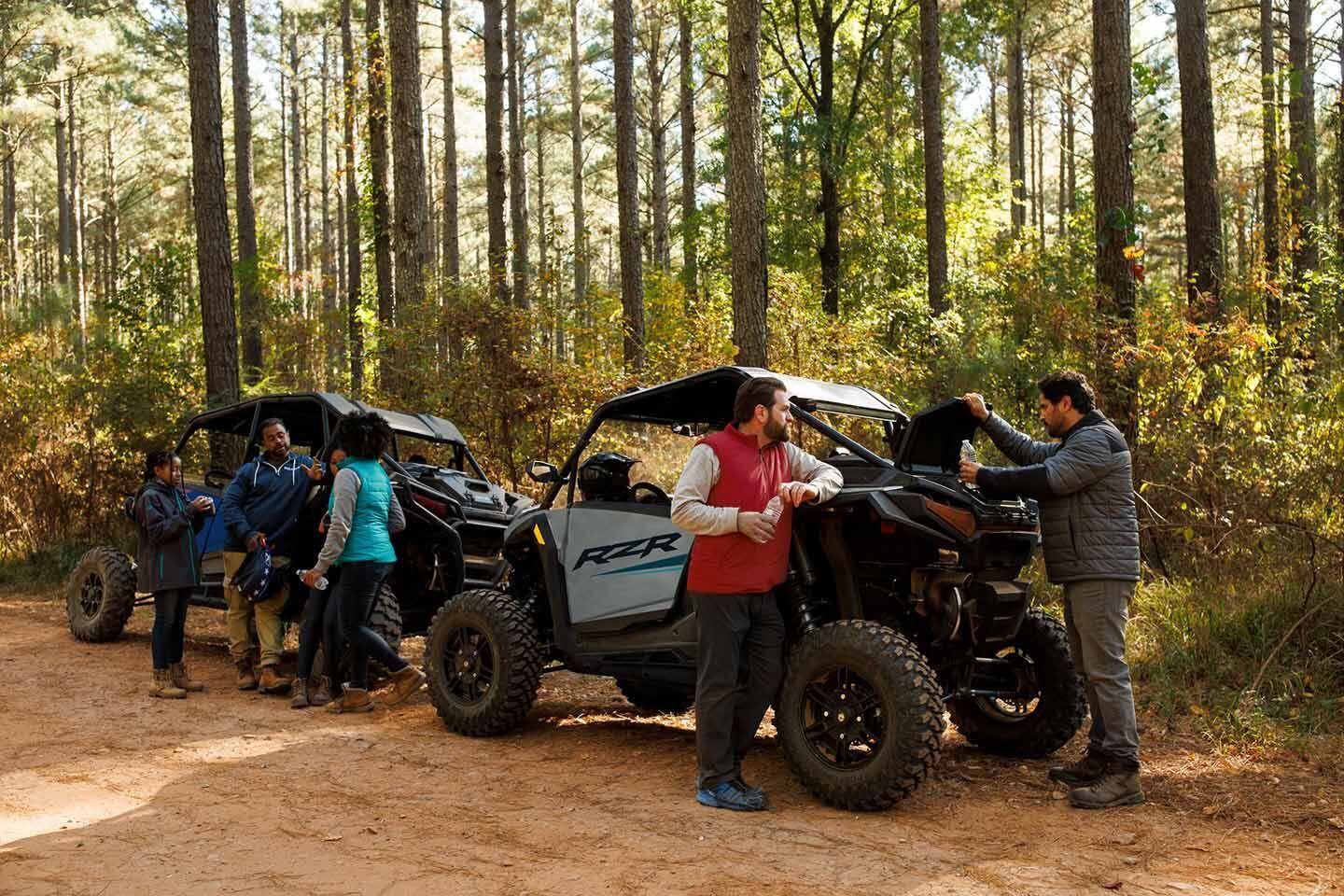 A group of people are standing next to atvs in the woods.